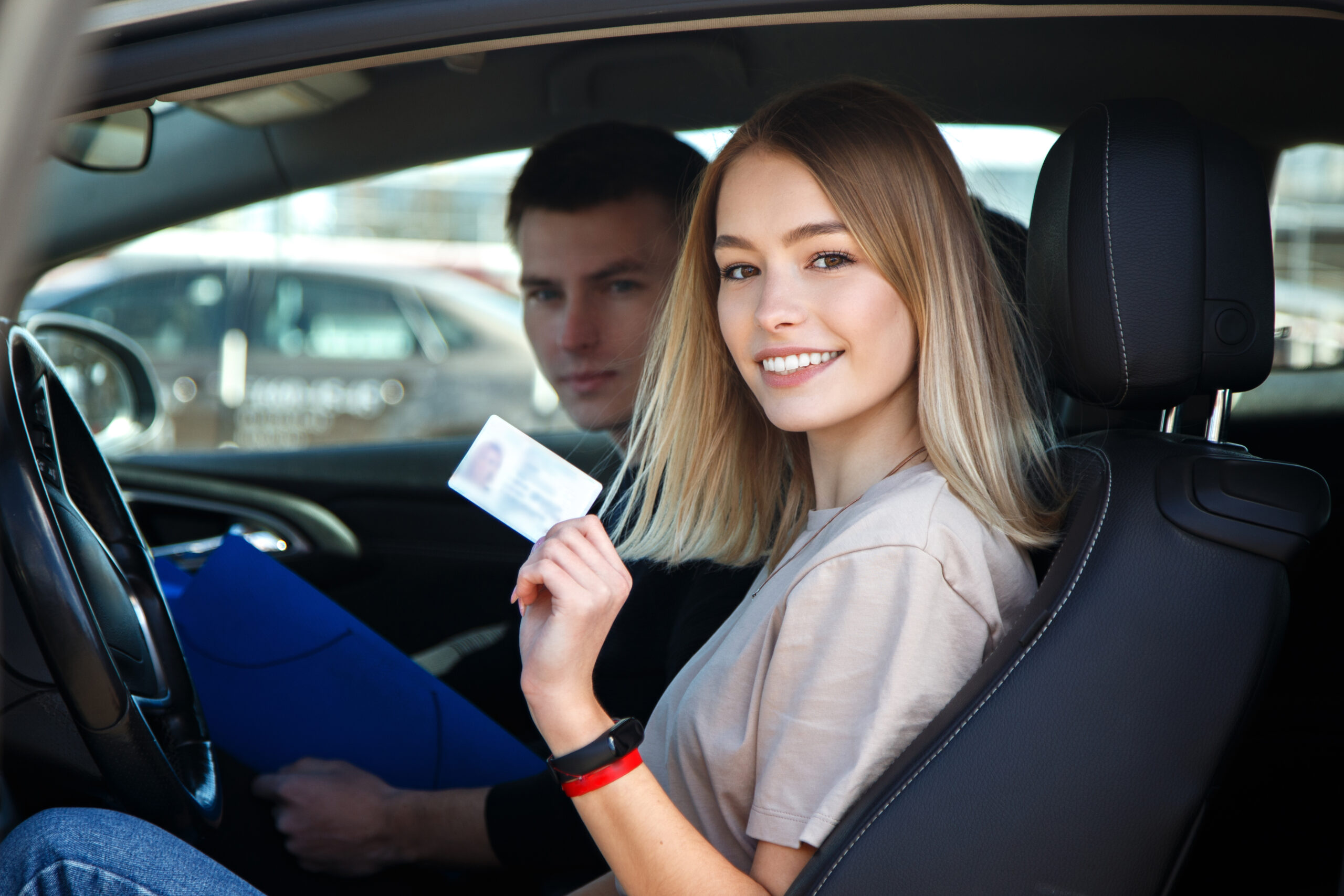 Joyful girl driving a training car with a drivers license card in her hands.